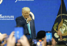 President Trump Delivers Remarks at FII Summit in Miami President Donald Trump delivering remarks at the FII Summit in Miami, standing on stage with the presidential seal and audience members capturing the moment on their smartphones.